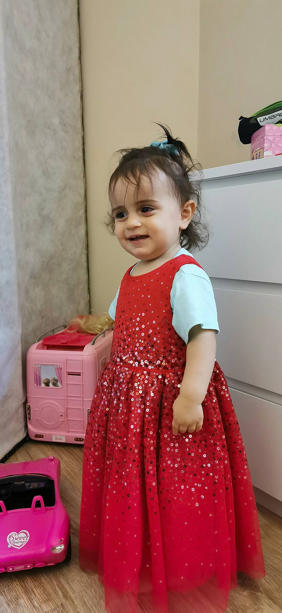 Asmin a rejoint le concours — aidez-le/la à gagner de superbes lots ! baby, baby_toddler_clothing, baggage, box, chest_of_drawers, child, curtain, day_dress, dress, embellishment, joy, one_piece_garment, person, pink, room, shelf, shelving, suitcase, toddler