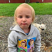 Charlee joined the competition — help win amazing prizes! toddler, child, hoodie, blond_hair, gravel, dog, pet, outdoor, grass, barn, fence, curious, expression, casual_clothing, young_child, nature, daylight, portrait, animal, small_dog