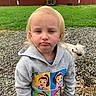 animal, barn, blond_hair, casual_clothing, child, curious, daylight, dog, expression, fence, grass, gravel, hoodie, nature, outdoor, pet, portrait, small_dog, toddler, young_child