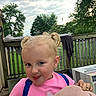 blonde_hair, blue_eyes, child, clothing, cloudy, cute, deck, hand, nature, outdoor, person, pigtails, pink_shirt, playful, sky, summer, toddler, tongue_out, trees, wooden_fence