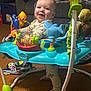 baby, smiling, indoor, activity_jumper, toys, sea_creatures, fish, shark, octopus, carpet, couch, child, happy, standing, playful, clothing, person, foot, head, colorful