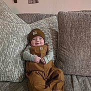 Hunter joined the competition — help win amazing prizes! baby, infant, smile, couch, cushion, brown_overalls, beanie, indoor, home_decor, wall_art, patterned_cushion, cute, child, person, seated, cozy, comfortable, happy, portrait, furniture