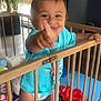 toddler, child, playpen, toys, indoor, wooden_bars, smiling, blue_shirt, barefoot, colorful, play_area, baby, cute, happy, person, young_child, furniture, plant, window, floor_mat