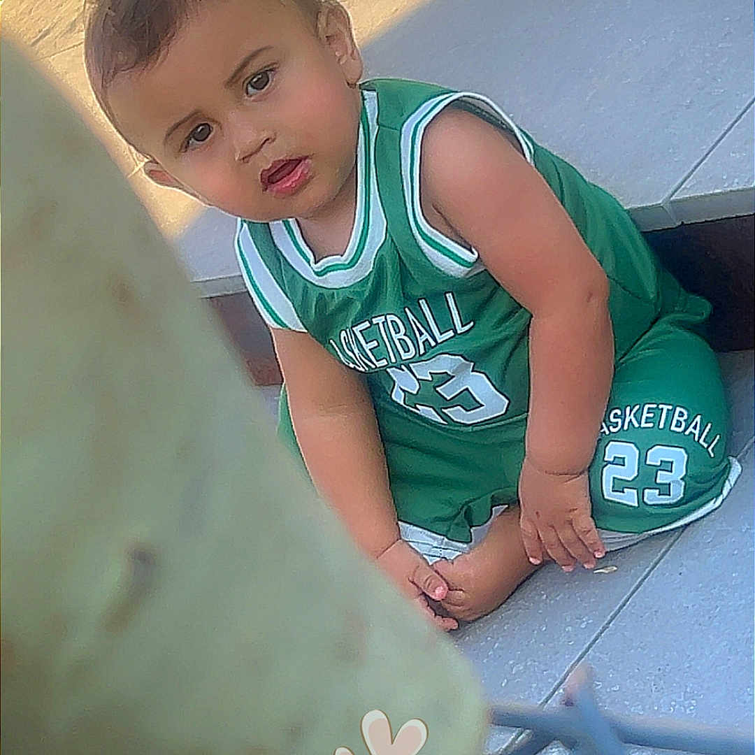 Alek participe au concours pour gagner de l'argent avec cette photo : barefoot, basketball_jersey, casual, child, curious, daytime, expression, floor, foreground_blur, green_clothing, heart_stickers, outdoor, person, short_hair, sitting, sportswear, sunlight, tiles, toddler, young_child
