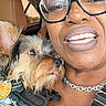 accessory, animal, black_hair, camouflage_clothing, car_interior, chain_necklace, closeup, cute, dog, friendship, glasses, happy, indoor, leather_seat, pet, portrait, seatbelt, small_dog, smile, woman