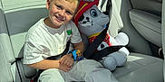 Jace is registered to the contest to win money with this photo: child, boy, smiling, car_interior, seat_belt, plush_toy, dalmatian, firefighter_hat, white_clothing, sneakers, watch, toy, seat, window, sunlight, happy, portrait, casual, backseat, vehicle