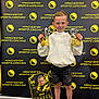 Jaxon joined the competition — help win amazing prizes! child, boy, trophies, sports_coaching, background, banner, trading_card, smile, standing, clothing, shorts, shoes, socks, portrait, indoor, award, celebration, happy, event, pose