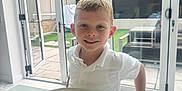 Jaxon is registered to the contest to win money with this photo: backyard, boy, child, corn_on_the_cob, food, freckles, glass_doors, indoor, ketchup, kitchen, marble_countertop, meal, outdoor_view, plate, potato_wedges, smiling, steak, table, white_polo, window