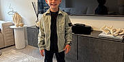 Jaxon joined the competition — help win amazing prizes! child, boy, smiling, standing, living_room, tv, reflection, jacket, sneakers, rug, modern, furniture, decor, watch, remote_control, window, curtains, table, sculpture, carpet