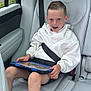 child, boy, car_seat, seatbelt, tablet, freckles, white_hoodie, shorts, sneakers, car_interior, road_trip, window, greenery, happy, smiling, technology, modern, seat, safety, casual_clothing
