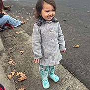 Scarlitt is registered to the contest to win money with this photo: building, casual_clothing, child, coat, curb, curly_hair, daytime, footwear, happy, leaves, outdoor, pavement, people, sidewalk, smiling, standing, street, toddler, traffic_light, urban