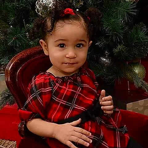Myasiya is registered to the contest to win money with this photo: child, toddler, portrait, sitting, smiling, thumbs_up, red_dress, plaid, christmas, christmas_tree, holiday, chair, indoors, ornaments, festive, curly_hair, hair_bows, family_photo, studio_photography, wooden_furniture
