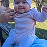 baby, child, infant, portrait, smiling, outdoor, park, trees, blanket, hat, knit_cap, pink_clothing, bodysuit, tights, sitting, adult_hands, daylight, nature, playful, family
