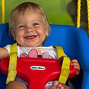 Hailee is registered to the contest to win money with this photo: baby, child, swing, smile, happy, outdoor, play, seat, yellow_straps, blue_swing, red_bar, person, feet, face, short_hair, earrings, clothing, green_background, toy, daylight