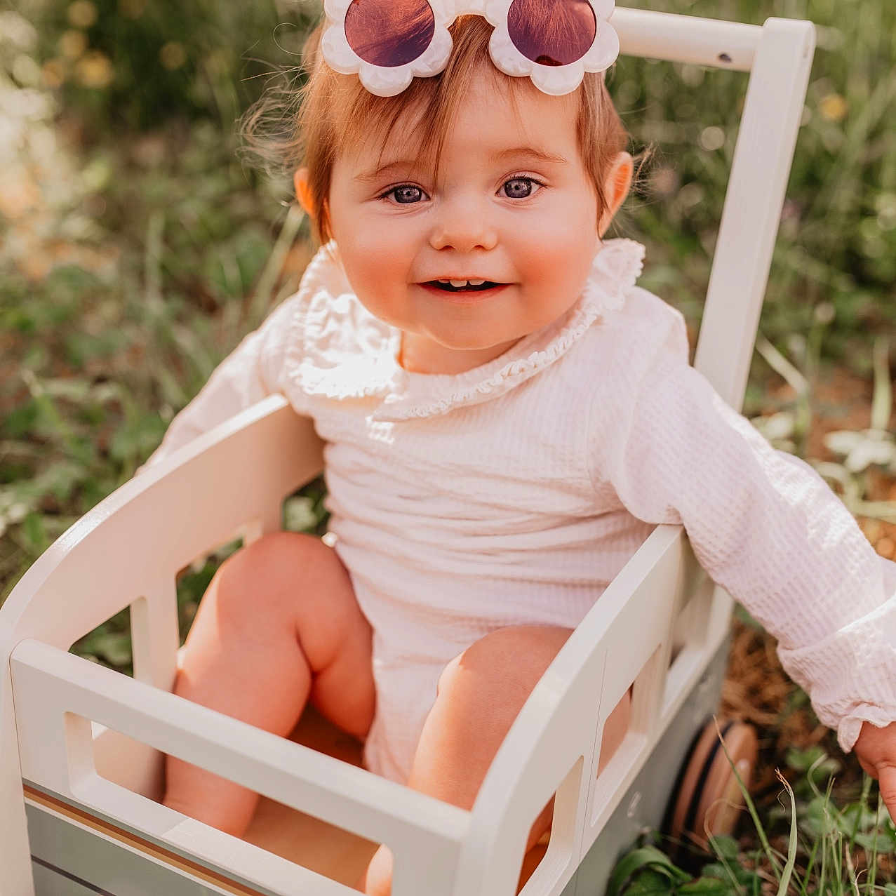 Flora participe au concours pour gagner de l'argent avec cette photo : baby, child, clothing, cute, face, flower_shaped, grass, greenery, happy, infant, nature, outdoor, person, playful, portrait, smiling, sunglasses, sunlight, toy_wagon, wooden_toy