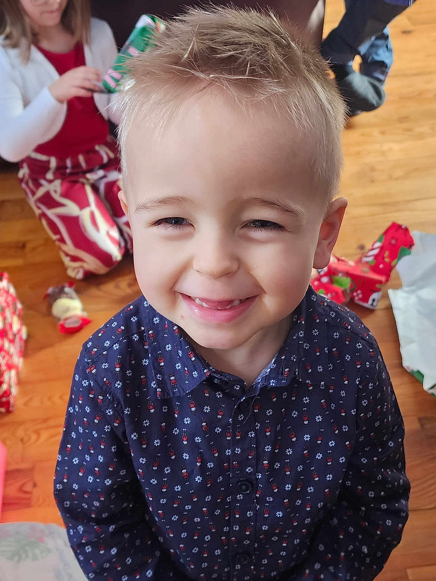 Esteban a rejoint le concours — aidez-le/la à gagner de superbes lots ! child, boy, smiling, happy, indoor, holiday, presents, gift_wrapping, floor, wooden_floor, shirt, patterned_clothing, blonde_hair, spiky_hair, girl, red_clothing, white_cardigan, family, celebration, portrait