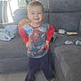child, boy, smiling, indoor, living_room, sofa, tiled_floor, barefoot, casual_clothing, spiderman_shirt, pants, furniture, curtains, flower_vase, toy, home, relaxed, portrait, happy, person