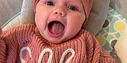 Elle is registered to the contest to win money with this photo: apparel, baby, checkered_floor, child, clothing, cushion, cute, expression, face, happy, headband, indoor, infant, knitted_clothing, person, pink_sweater, portrait, seated, small_child, smiling