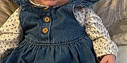 Elle is registered to the contest to win money with this photo: baby, child, denim_dress, buttons, couch, cushion, happy, smiling, face, eyes, hand, long_sleeve_shirt, patterned_clothing, indoor, plush, soft_fabric, portrait, sitting, cute, infant
