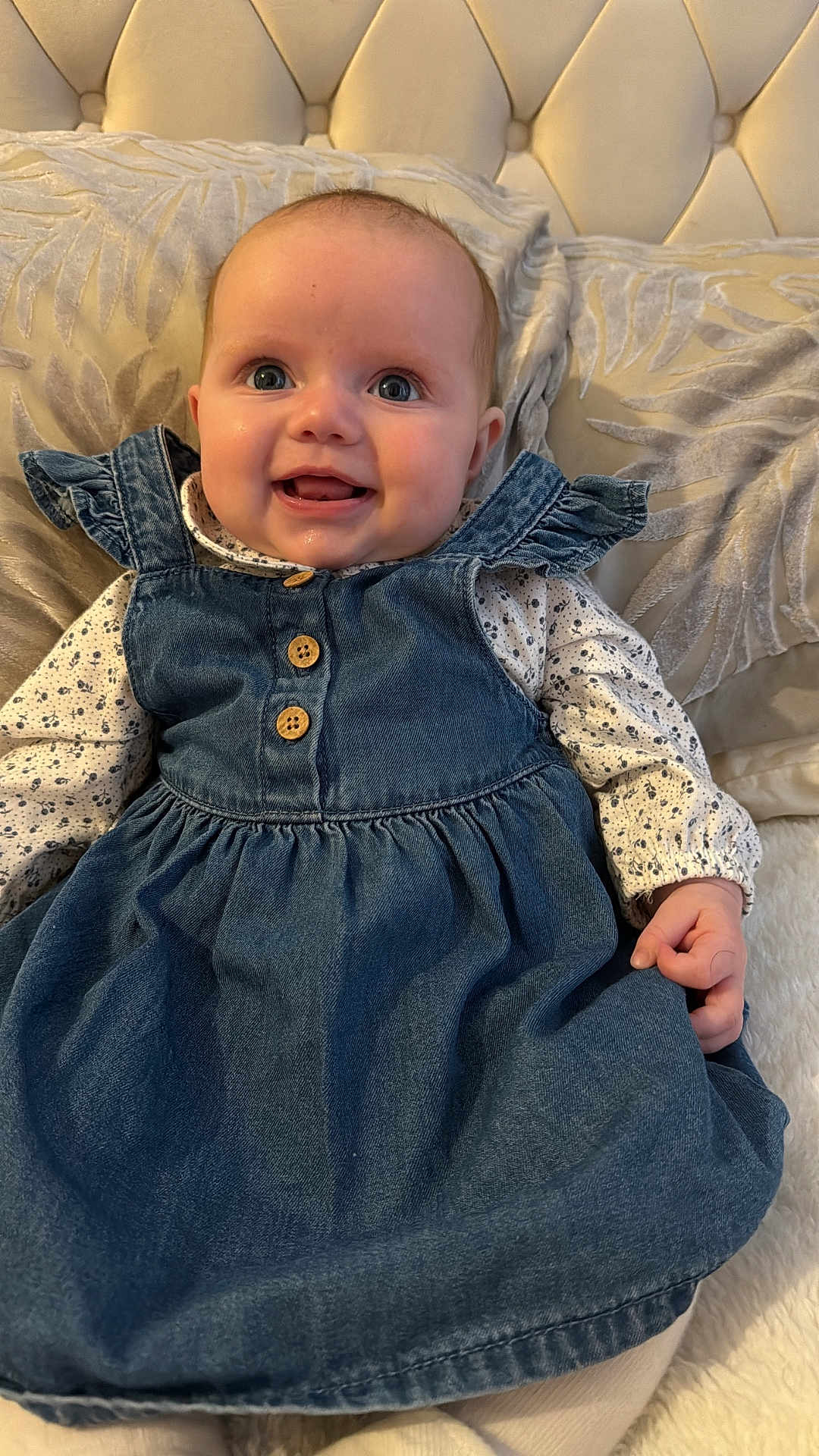 Elle is registered to the contest to win money with this photo: baby, child, denim_dress, buttons, couch, cushion, happy, smiling, face, eyes, hand, long_sleeve_shirt, patterned_clothing, indoor, plush, soft_fabric, portrait, sitting, cute, infant