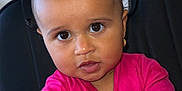 Sòul is registered to the contest to win money with this photo: toddler, child, baby, pink_clothing, face, portrait, chair, curly_hair, earrings, indoor, skin, hands, looking_at_camera, young_child, sitting, expression, casual_clothing, person, cute, small_pony_tail