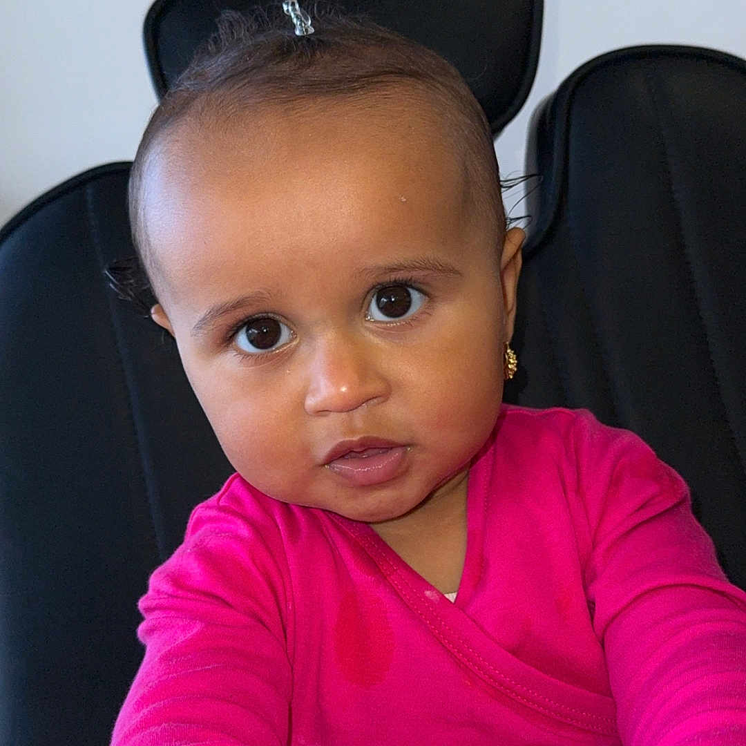 Sòul is registered to the contest to win money with this photo: baby, casual_clothing, chair, child, curly_hair, cute, earrings, expression, face, hands, indoor, looking_at_camera, person, pink_clothing, portrait, sitting, skin, small_pony_tail, toddler, young_child