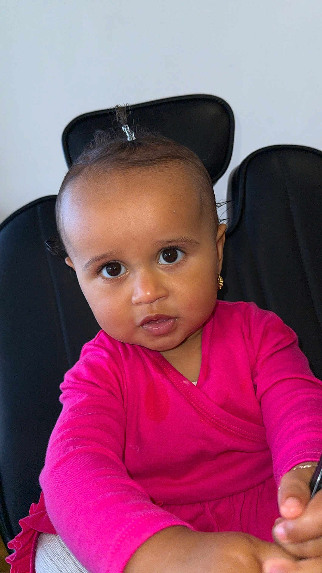 Sòul is registered to the contest to win money with this photo: toddler, child, baby, pink_clothing, face, portrait, chair, curly_hair, earrings, indoor, skin, hands, looking_at_camera, young_child, sitting, expression, casual_clothing, person, cute, small_pony_tail