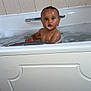 baby, bathtub, bath, bubbles, child, ears, foam, gold_earrings, looking, portrait, soap, tile_wall, water, wet_skin, young_child, indoor, bathroom, sitting, curious, face