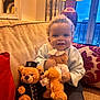 toddler, child, smiling, indoor, couch, teddy_bear, toy, lamp, window, curtain, pillow, clothing, face, hair, socks, furniture, home, cozy, happy, person