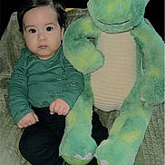 Thiago joined the competition — help win amazing prizes! baby, child, dinosaur, plush_toy, green, socks, blanket, indoor, cute, portrait, seated, young, face, clothing, toy, soft, cozy, expression, black_pants, hands