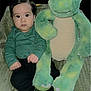 baby, child, dinosaur, plush_toy, green, socks, blanket, indoor, cute, portrait, seated, young, face, clothing, toy, soft, cozy, expression, black_pants, hands