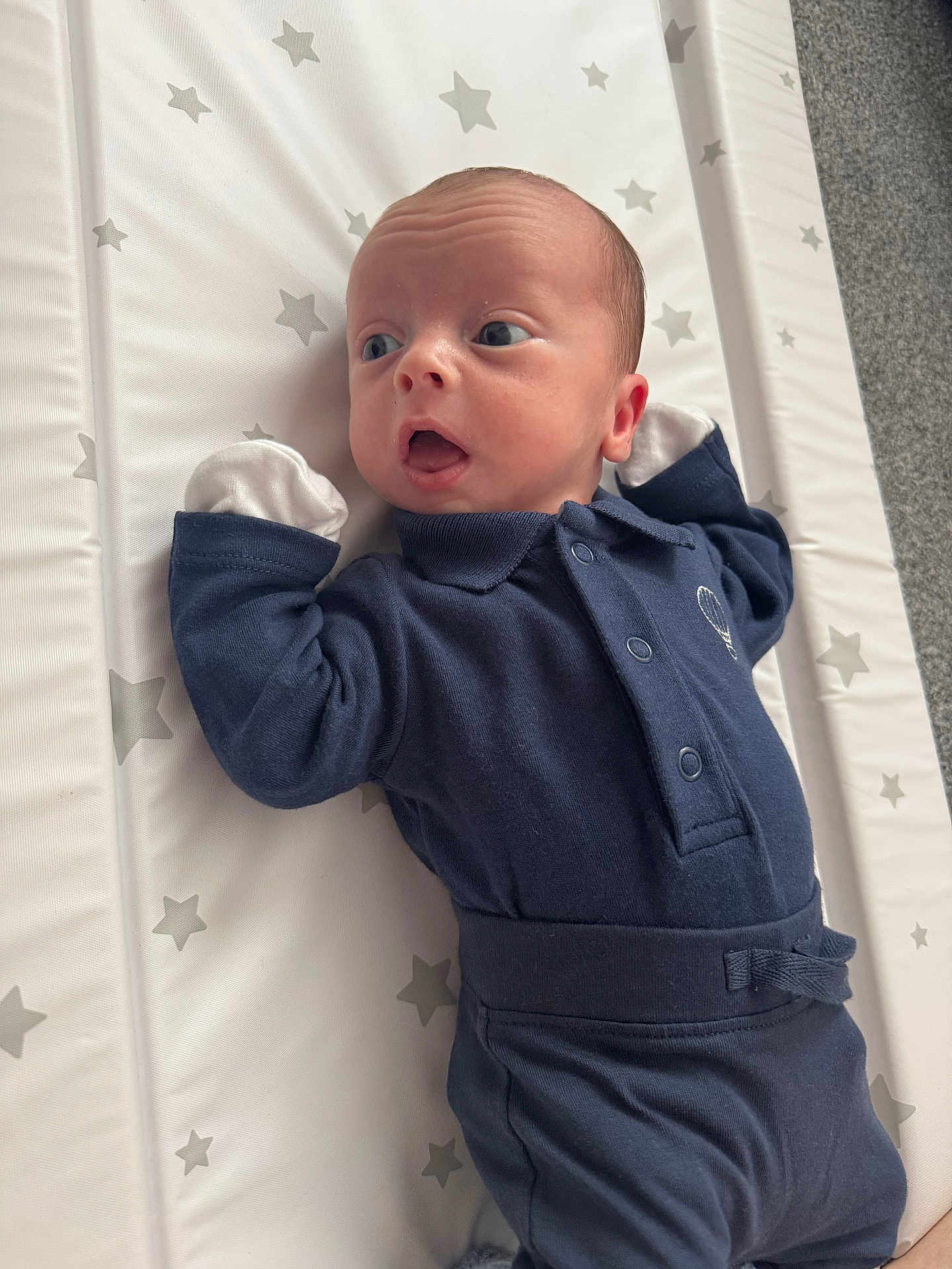 Jaxxon-Brian is registered to the contest to win money with this photo: baby, infant, newborn, blue_outfit, mittens, star_pattern, mattress, curious, wide_eyes, lying_down, soft_lighting, indoor, child, young, cute, small_hands, facial_expression, cozy, portrait, person