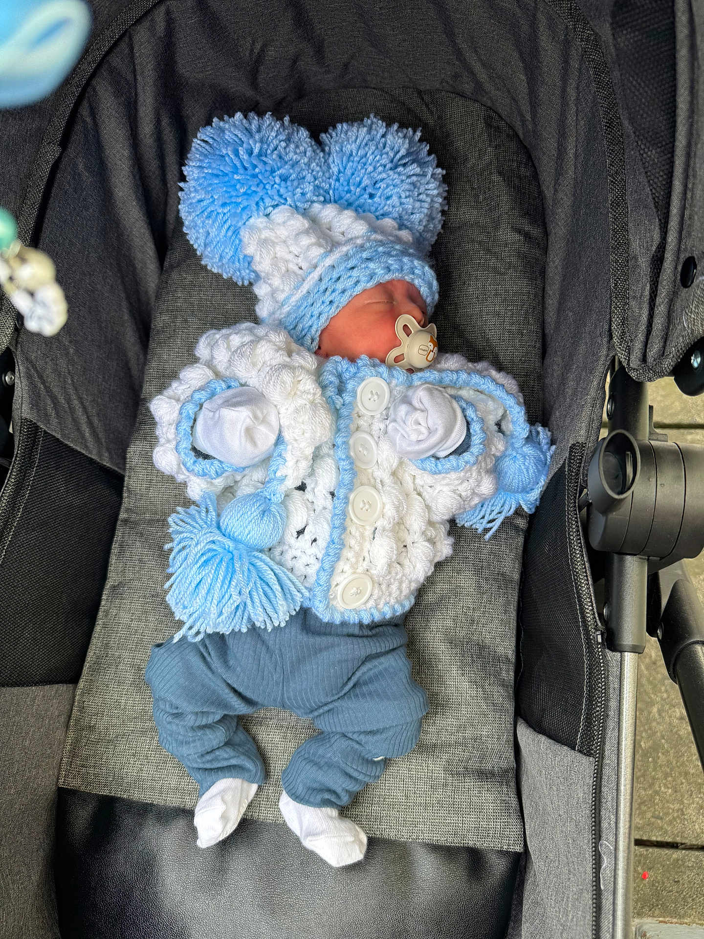 Jaxxon-Brian is registered to the contest to win money with this photo: baby, blue, child, clothing, cozy, cute, fabric, infant, knitted_hat, knitted_sweater, newborn, outdoor, pacifier, pom_poms, resting, sleeping, soft, stroller, warm, white