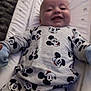 apparel, baby, bed, changing_pad, child, clothing, cute, face, happy, indoor, infant, lying_down, mickey_mouse, onesie, pattern, person, smiling, soft, star_pattern, young