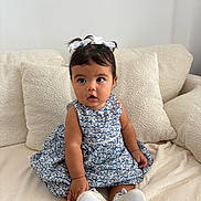 Alba a rejoint le concours — aidez-le/la à gagner de superbes lots ! toddler, child, girl, dress, blue_and_white, floral_pattern, white_bows, hair_accessories, white_shoes, couch, pillows, blanket, indoor, sitting, curious, wide_eyes, cute, portrait, baby, soft_lighting