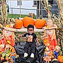 Joshua is registered to the contest to win money with this photo: autumn, bench, black_clothing, child, cornstalk, decorations, fall, festival, grass, hat, holiday, orange, outdoor, pacifier, pumpkin, scarecrow, seasonal, smiling_face, toddler, welcome_sign