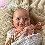 baby, smiling, face, blanket, onesie, floral_pattern, infant, cozy, cute, child, happy, skin, hand, lying_down, soft_texture, bed, comfort, portrait, indoors, young_child