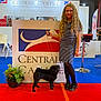 Saint Maxime participe au concours pour gagner de l'argent avec cette photo : girl, child, dog, pug, leash, exhibition_booth, signage, indoor, carpet, blue_carpet, red_carpet, plant, shoes, dress, glasses, long_hair, smile, portrait, event, dog_show