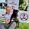 black_dog, collar, dog, festival, girl, glasses, grass, happy, holding, outdoor, pet_show, photography, portrait, pug, royal_canin, signage, sitting, smile, trees, youth