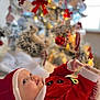 baby, blurred_background, celebration, child, christmas_tree, cute, decorations, festive, holiday, indoors, infant, lights, ornaments, portrait, reaching, red_clothing, santa_hat, smiling, soft_texture, winter