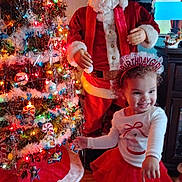 Mila is registered to the contest to win money with this photo: birthday_girl, cabinet, celebration, child, christmas_tree, curly_hair, decorations, festive, floor, happy, holiday, indoors, lights, ornaments, red_skirt, santa_claus, smiling, tinsel, toy, white_top