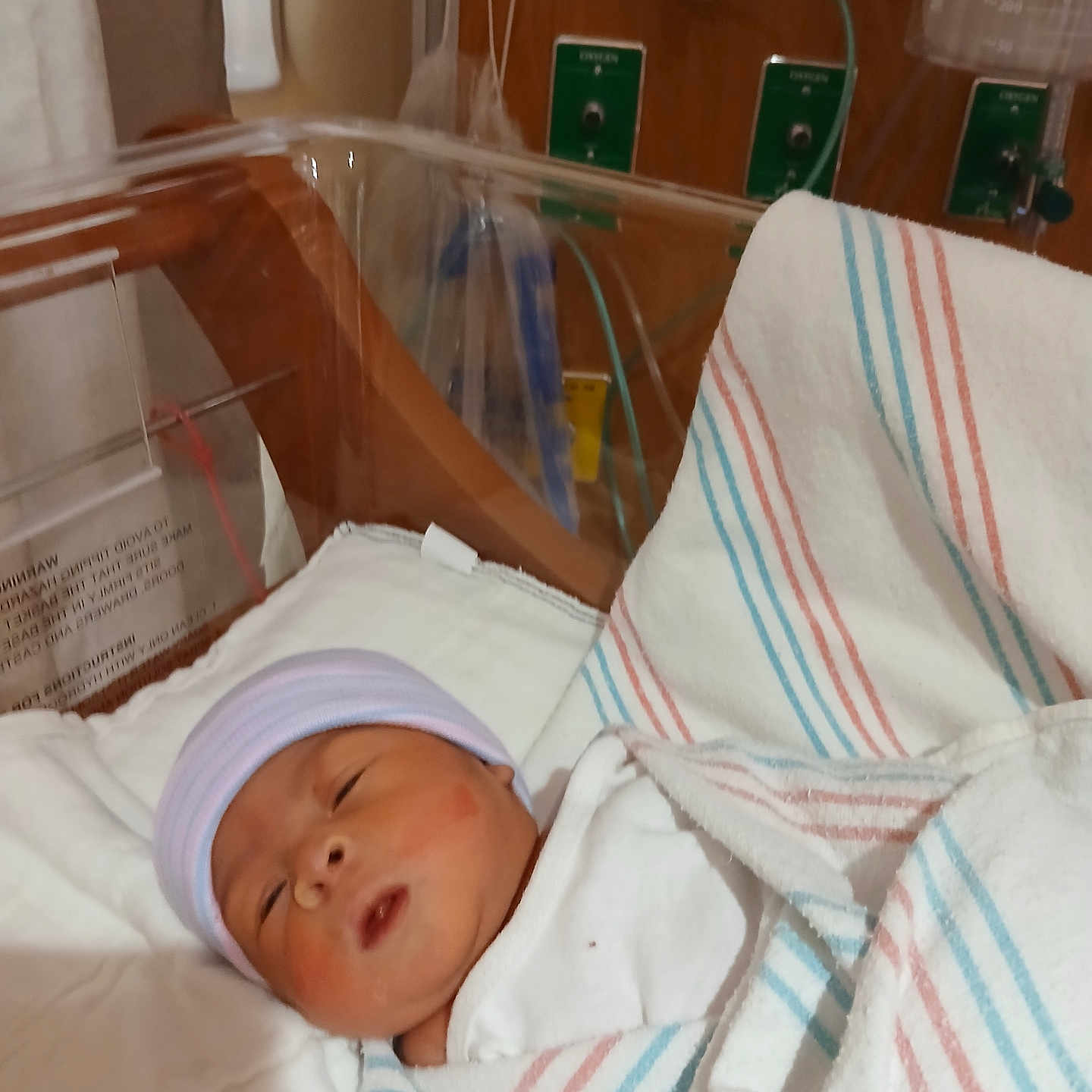 Kennedi is registered to the contest to win money with this photo: newborn, baby, hospital, bassinet, blanket, hat, medical_equipment, sleeping, infant, bed, healthcare, patient, nursery, person, wrapped, cozy, cute, indoor, quiet, resting