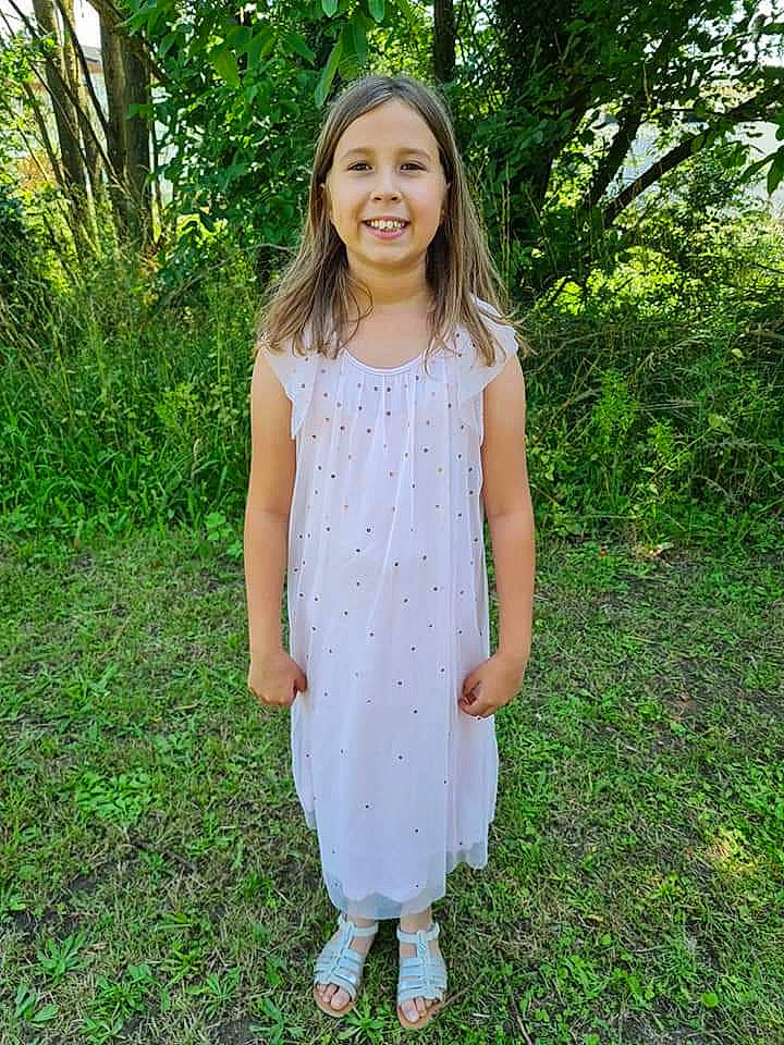 Héléna a rejoint le concours — aidez-le/la à gagner de superbes lots ! baby_toddler_clothing, brown_hair, day_dress, dress, facial_expression, grass, hair, happy, joy, long_hair, neck, one_piece_garment, pattern, people_in_nature, person, plant, shoulder, sleeve, smile, toddler