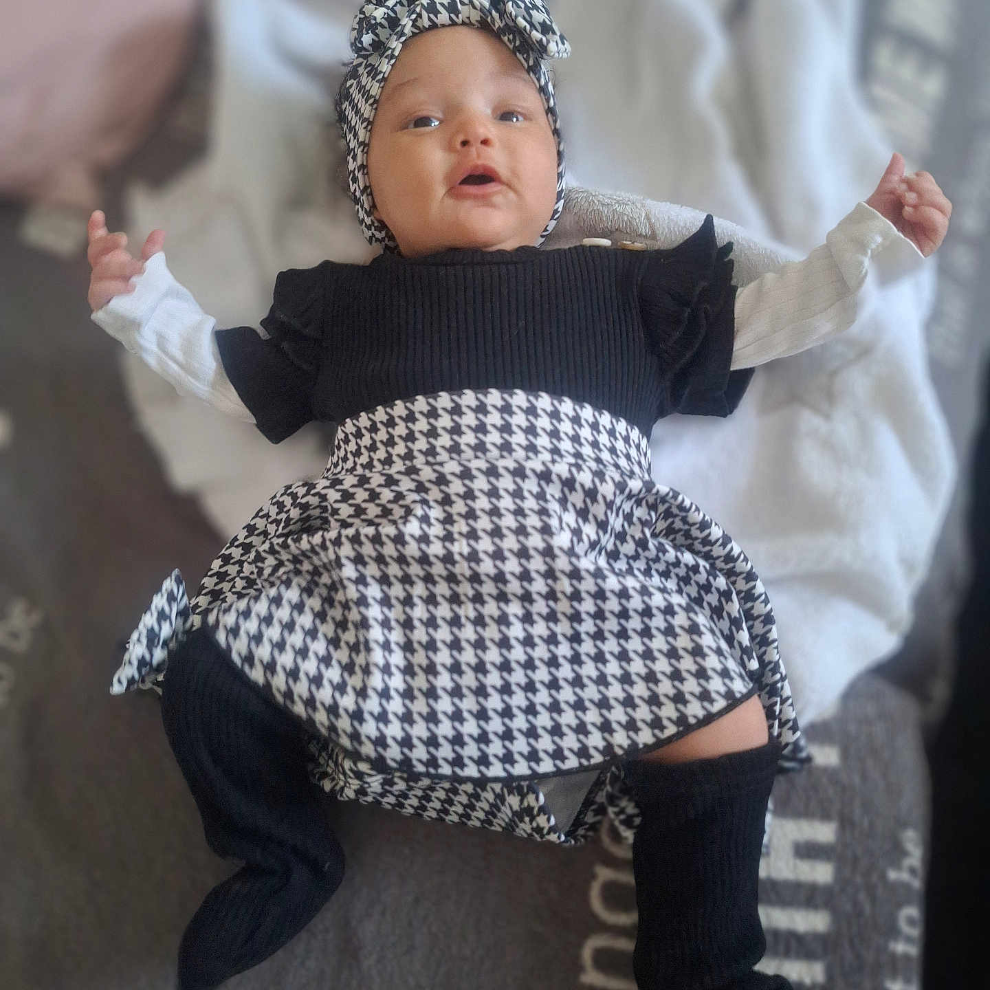 Alayna a rejoint le concours — aidez-le/la à gagner de superbes lots ! arms_outstretched, baby, black_and_white, blanket, child, clothing, cozy, cute, face, fashion, headband, houndstooth, indoor, infant, leg_warmers, lying_down, person, portrait, sock, soft_focus