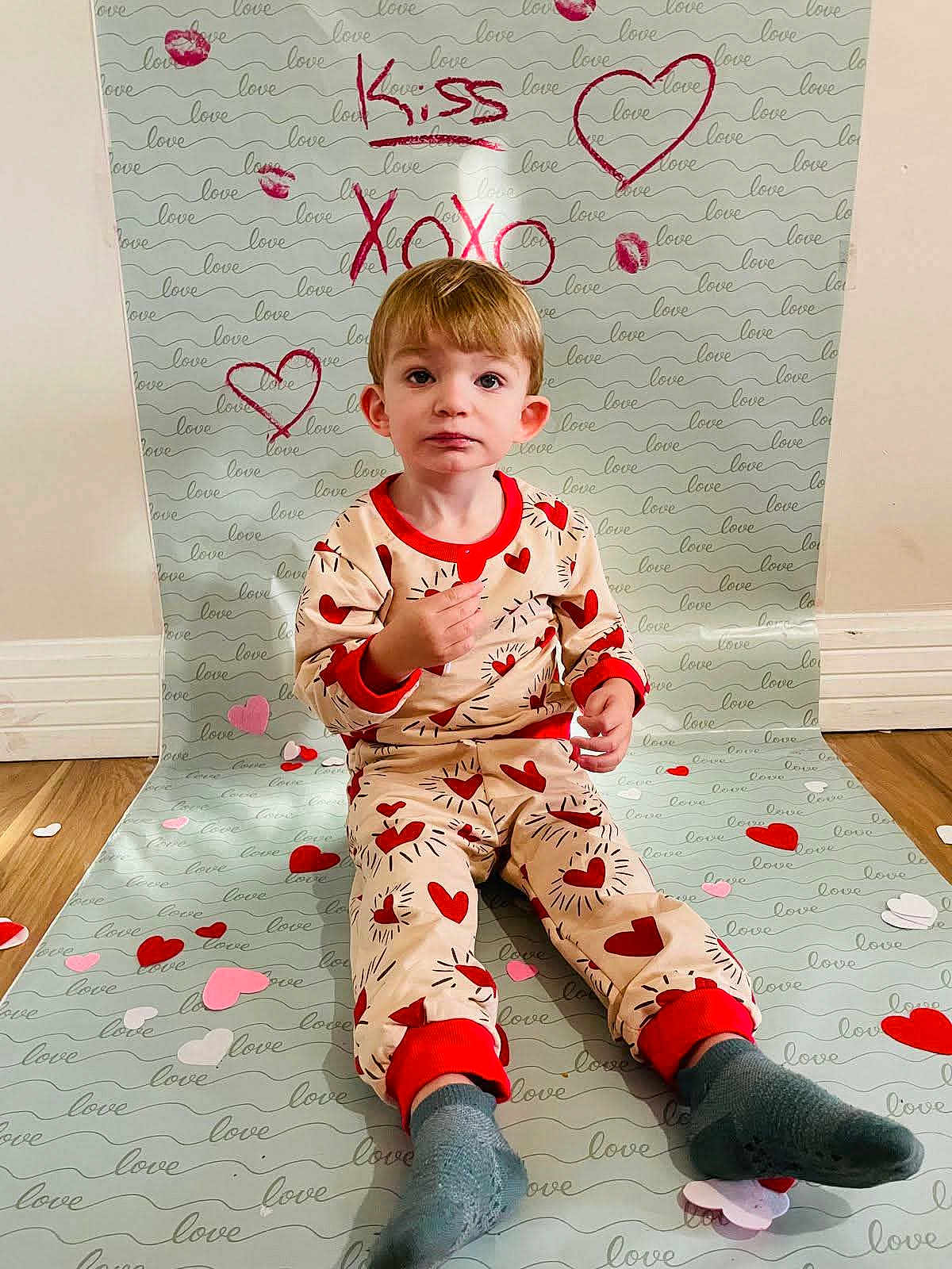 Hunter joined the competition — help win amazing prizes! child, toddler, boy, pajamas, heart_pattern, valentine_backdrop, sitting, socks, hardwood_floor, paper_hearts, love_text, kiss_text, backdrop, wall, portrait, indoor, cute, expression_neutral, flooring, studio_setup