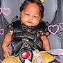 Keilani joined the competition — help win amazing prizes! baby, car_seat, child, infant, heart_effects, bow, clothing, straps, black_and_gold, cute, adorable, indoors, safety_harness, pacifier_clip, patterned_outfit, pink_hearts, seatbelt, headrest, young_child, portrait