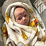 baby, blanket, infant, face, wrapped, cushion, seat, warning_label, soft_texture, indoors, cute, child, newborn, closeup, expression, warm, comfort, person, portrait, fabric