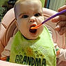 Roselynn is registered to the contest to win money with this photo: baby, child, feeding, spoon, high_chair, bib, green_bib, pink_high_chair, indoor, person, face, mouth_open, hand, clothing, cute, expression, home, infant, smile, feeding_time