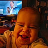 baby, smile, face, indoor, television, screen, table, wood, living_room, furniture, child, person, clothing, happy, home, light, closeup, candid, entertainment, cozy