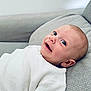 baby, infant, smile, happy, face, white_clothing, knitwear, couch, gray_fabric, indoors, person, head, skin, cute, child, lying_down, closeup, young, cozy, comfort